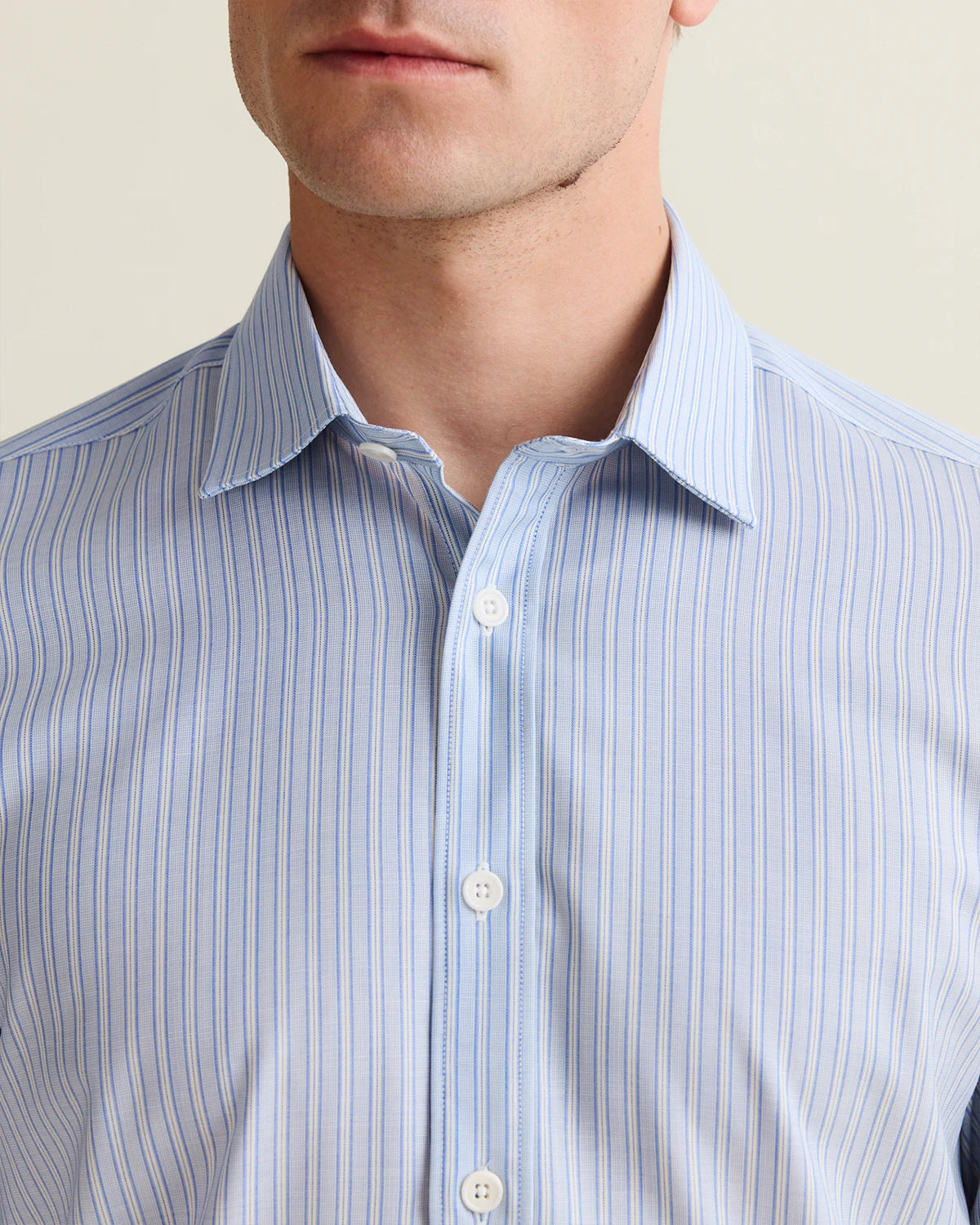 Close-up of a person wearing a light blue striped merino shirt against a neutral background with open collar