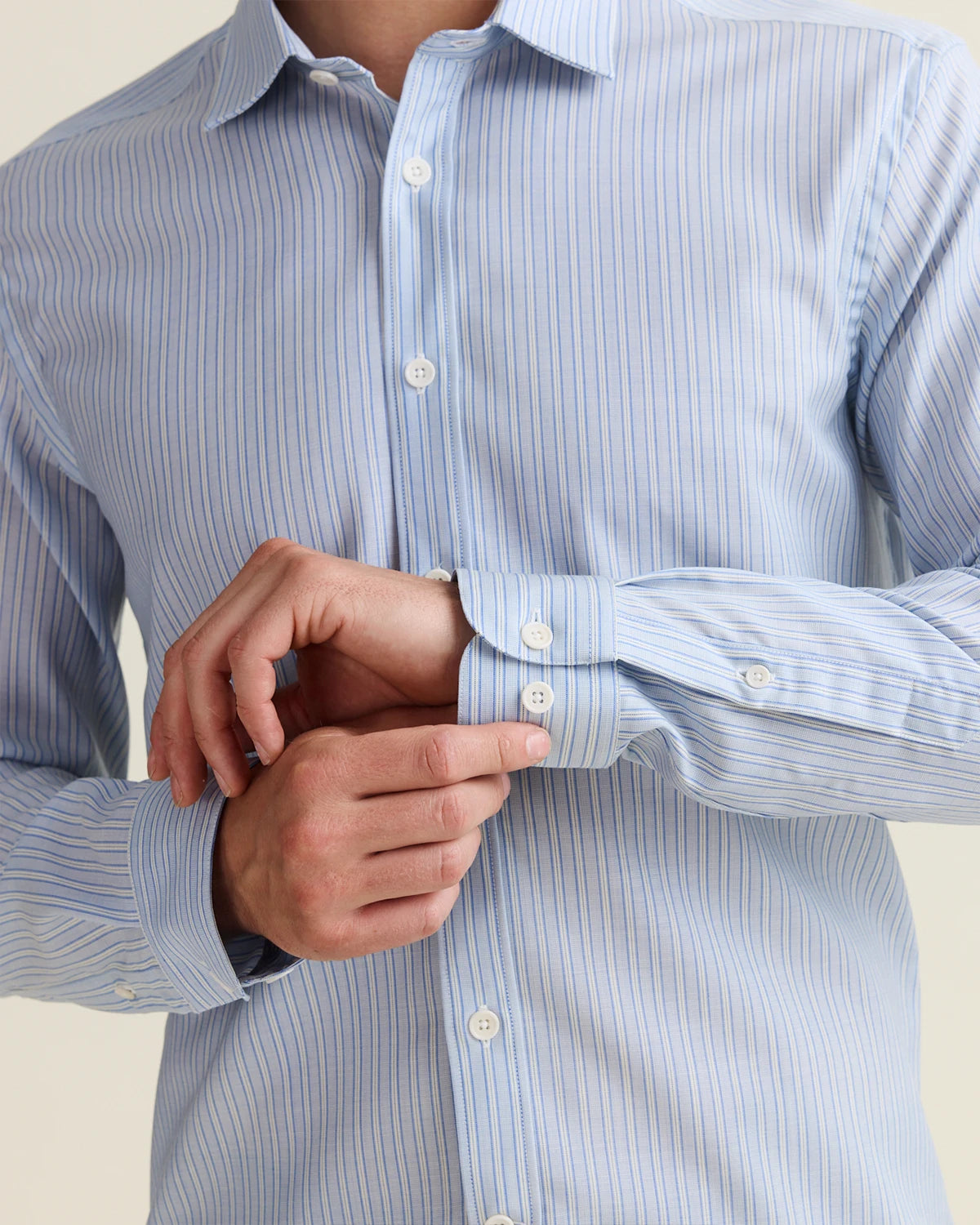 Close-up of cuff details and corozo buttons of a light blue merino striped shirt worn by a person