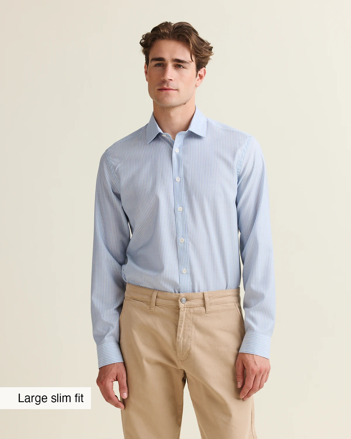 Man wearing a light blue striped merino shirt tucked in a beige pants on a plain background