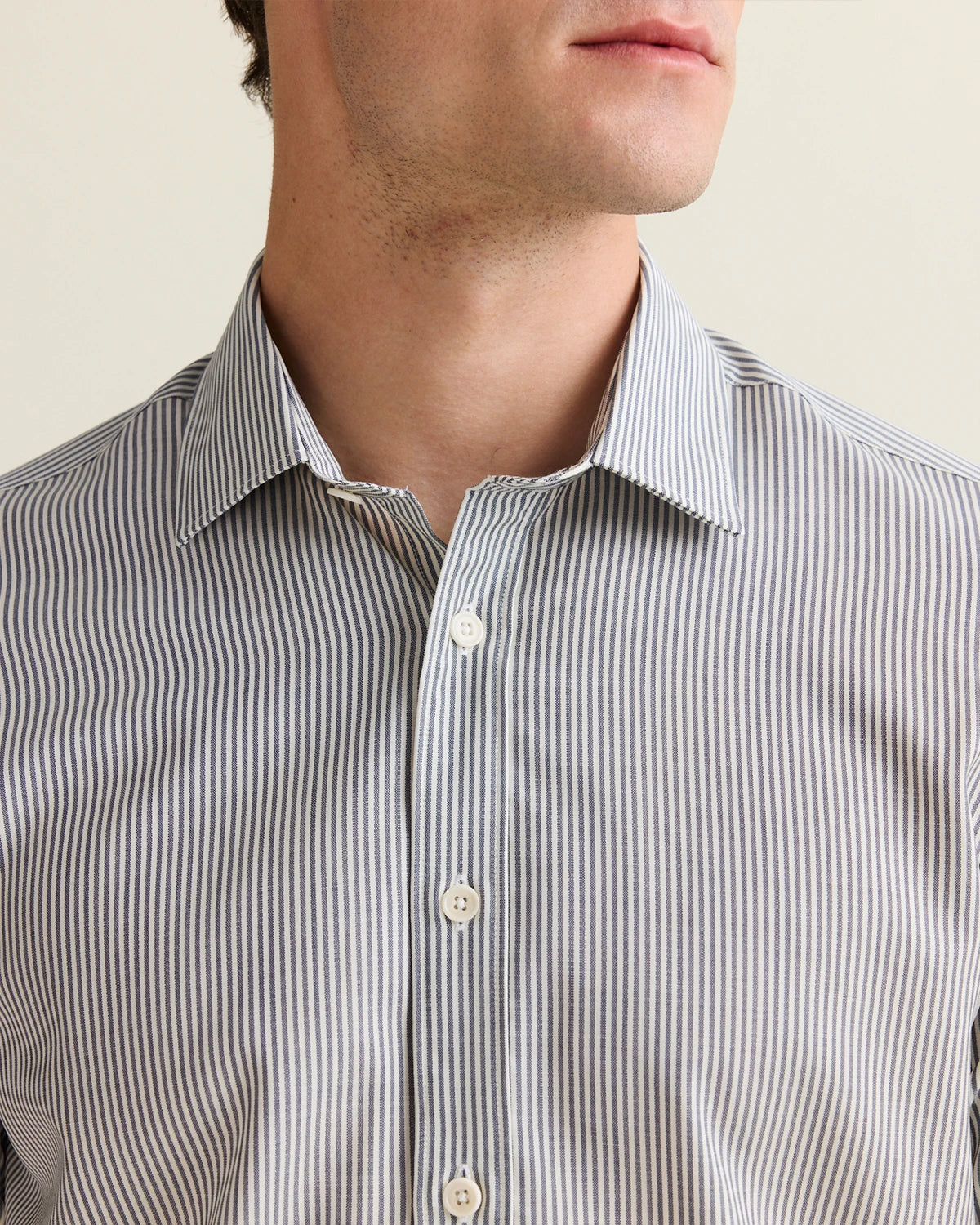 Close-up of a man wearing a navy striped merino shirt with a neutral background