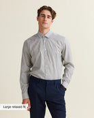 Man wearing a navy bengal striped dress shirt in merino wool tucked in on a dark blue pants on a beige background.