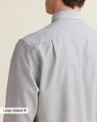 Close-up of of the back shoulder of a person wearing a navy bengal striped shirt against a beige background