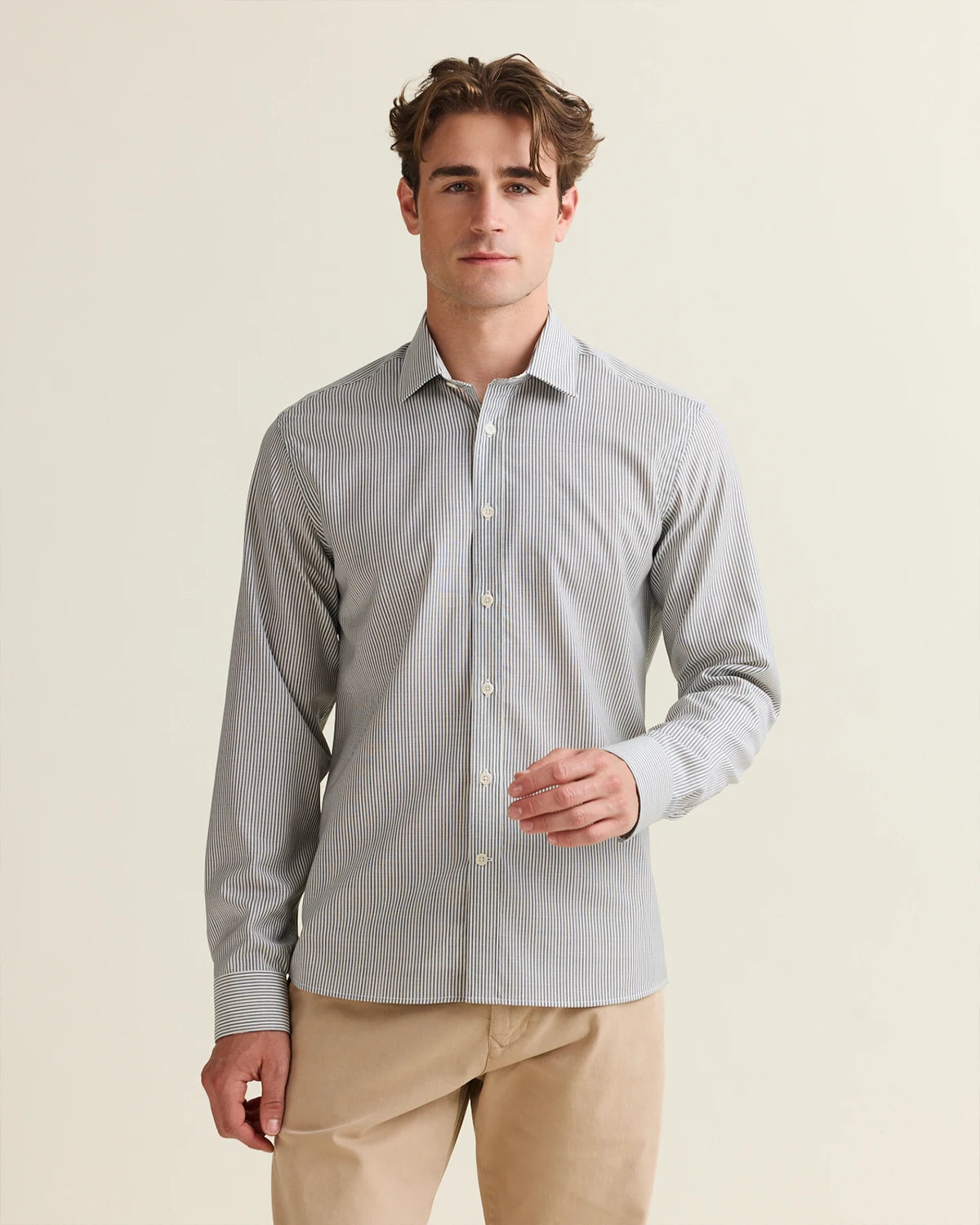 Man wearing a navy bengal striped merino wool shirt and beige pants on a beige background