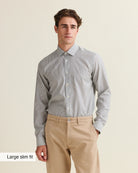 Man wearing a navy bengal striped merino shirt tucked in and beige pants on a beige background