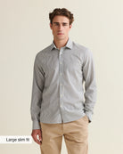 Front view of a man wearing a navy bengal striped merino wool shirt and beige pants on a beige background