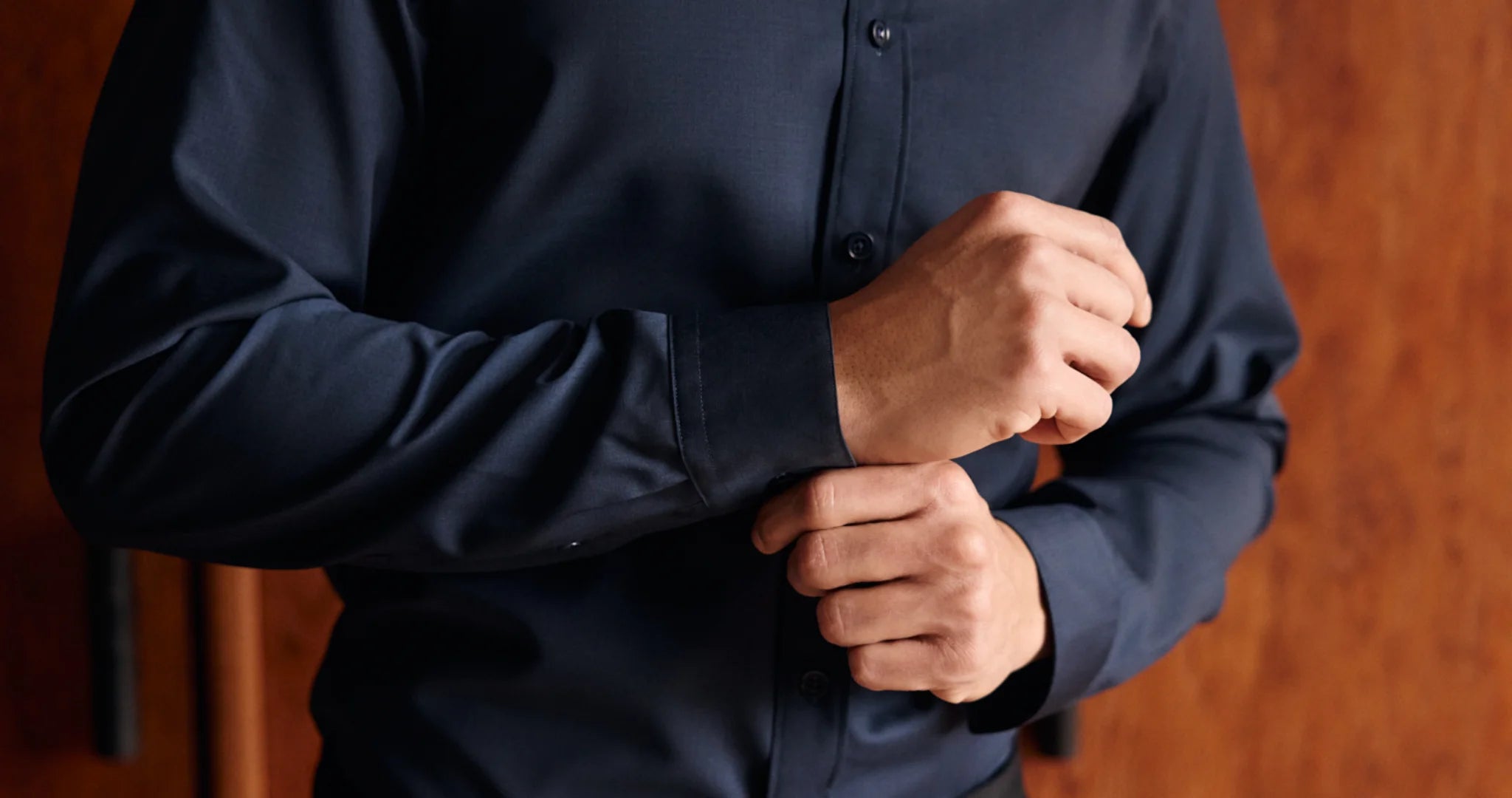Person wearing a dark blue merino wool shirt with a blurred background showing cuff detals