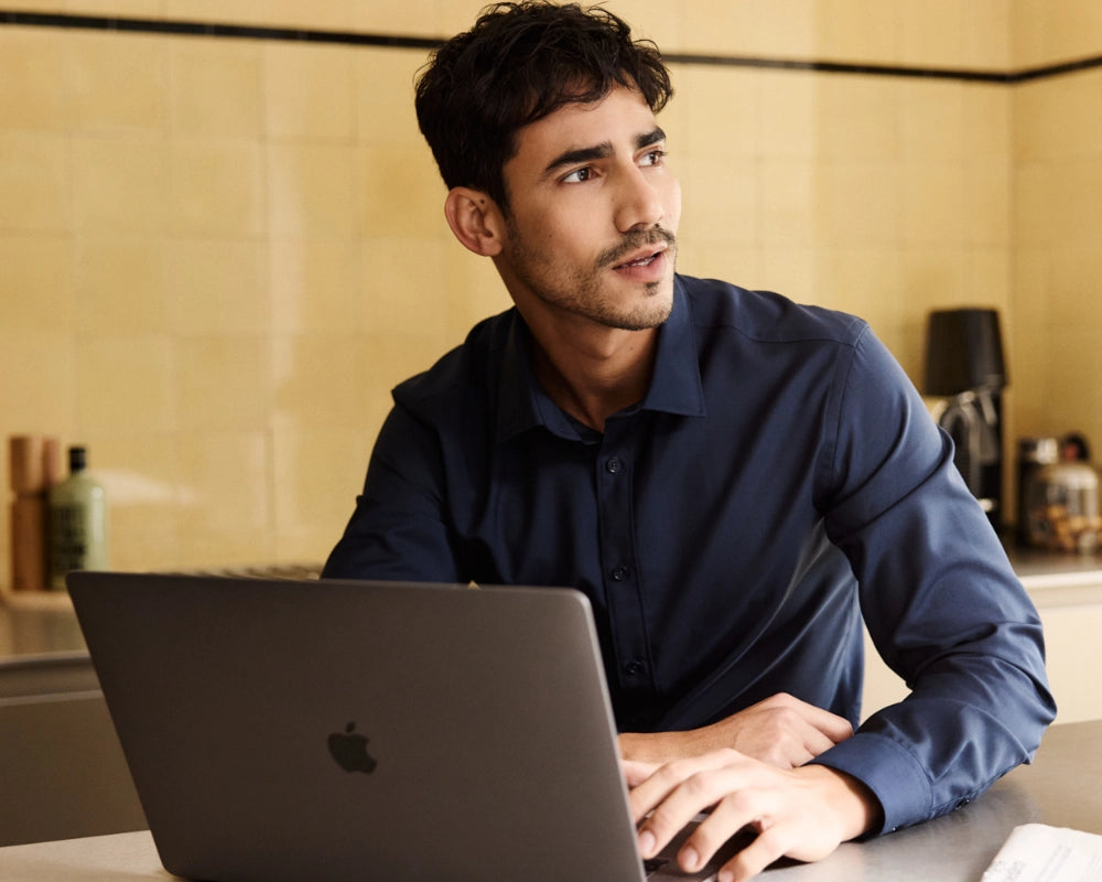 Man wearing a navy blue merino shirt from Wolk and using a laptop in a kitchen setting