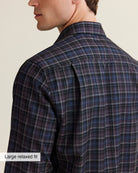 Close up of back shoulder of A man wearing a long-sleeve plaid button-down shirt in dark blue, purple, and gray.