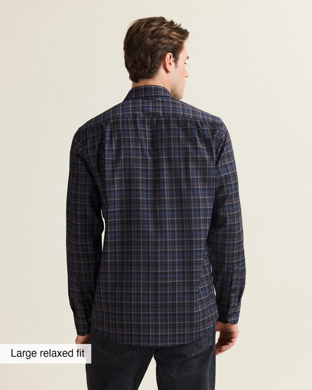 A man shown from the back wearing a dark navy and black plaid Wolk merino shirt, paired with dark jeans. The image has a text overlay in the bottom-left corner that reads 'Large relaxed fit'.