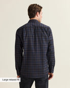 A man shown from the back wearing a dark navy and black plaid Wolk merino shirt, paired with dark jeans. The image has a text overlay in the bottom-left corner that reads 'Large relaxed fit'.