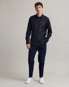 A man modeling a dark navy blue long-sleeve button-down shirt and matching navy trousers, paired with white sneakers, against a neutral light gray studio background.