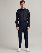 A man modeling a dark navy blue long-sleeve button-down merino wool shirt and matching navy trousers, paired with white sneakers, against a neutral light gray studio background.