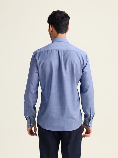 Backview of man wearing a light blue denim merino wool shirt with long sleeves untucked on a navy pants