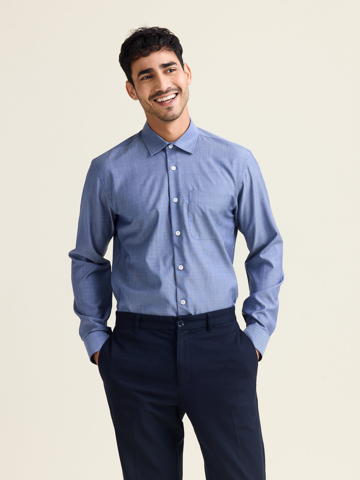 Man wears a merino wool shirt in light blue denim color with chest pocket and white buttons tucked in dark navy pants