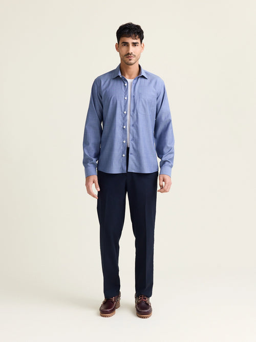Man wears a merino wool shirt in light blue denim color with chest pocket and white buttons open on a white merino wool T-shirt and on a dark navy pants