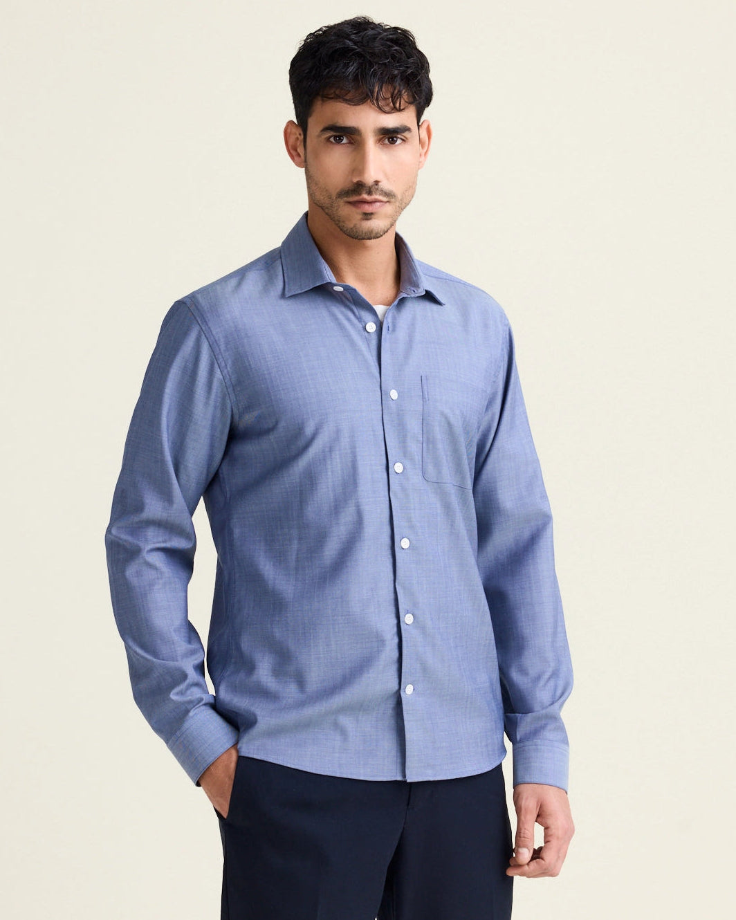 Man wears a merino wool shirt in light blue denim color with chest pocket and white buttons untucked on a navy pants