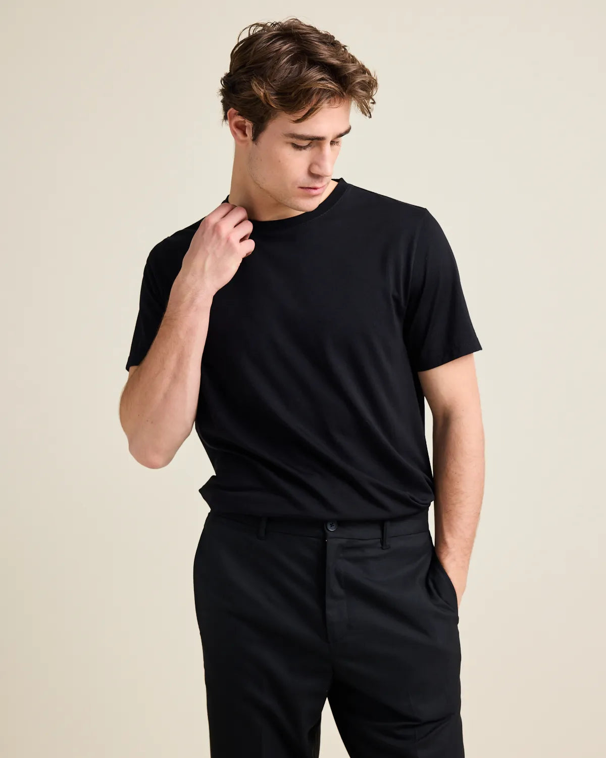 Man wearing a black merino t-shirt from Wolk and black pants against a beige background
