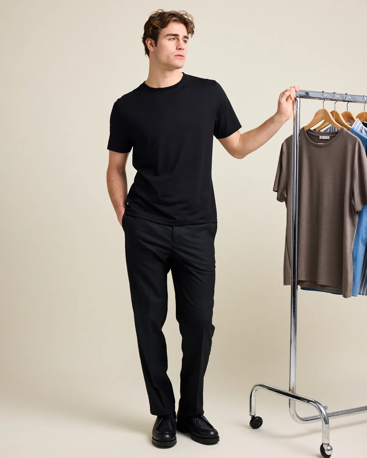 Man in black outfit standing next to a clothing rack with other shirts.