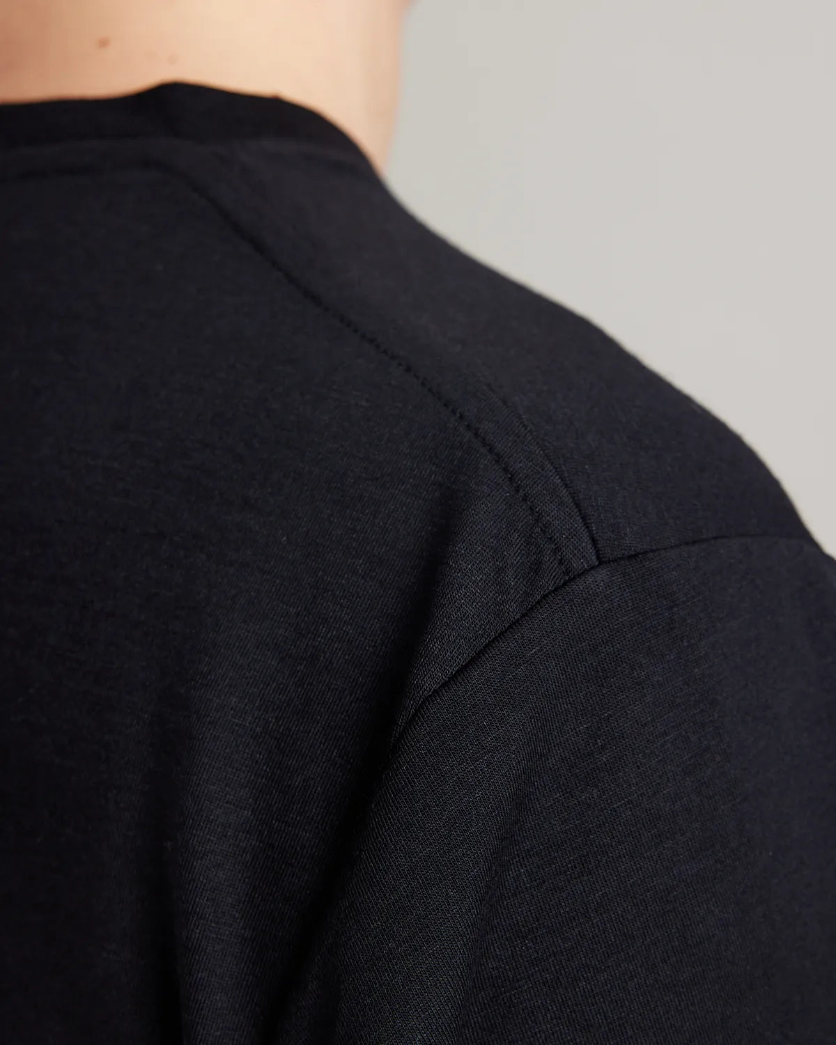 Close-up of the shoulder seam on a black merino T-shirt, showing the jersey texture