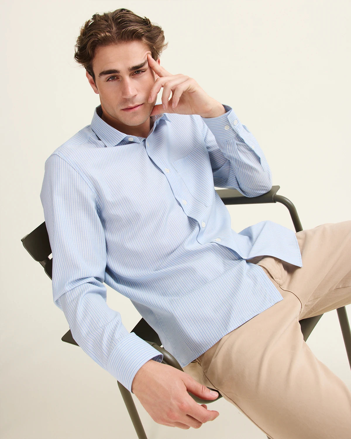 Man sitting on a chair wearing a light blue striped merino wool shirt with chest pocket from Wolk and beige pants.