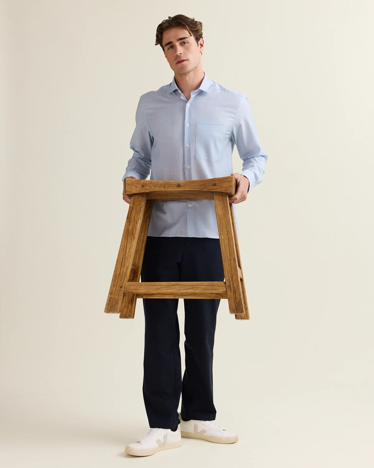 Man holding a wooden stool against a plain background