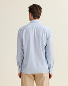 Back view of Man wearing a light blue striped merino wool shirt with long sleeves and beige pants on a plain background