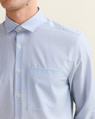 Close-up of the chest pocket and merino wool fabric of a person wearing a light blue striped shirt against a neutral background
