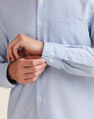 Close-up of a person adjusting the cuff of a light blue striped merino wool shirt.