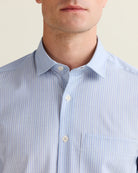 Close-up of the open collar of a person wearing a light blue striped merino wool shirt with a neutral background