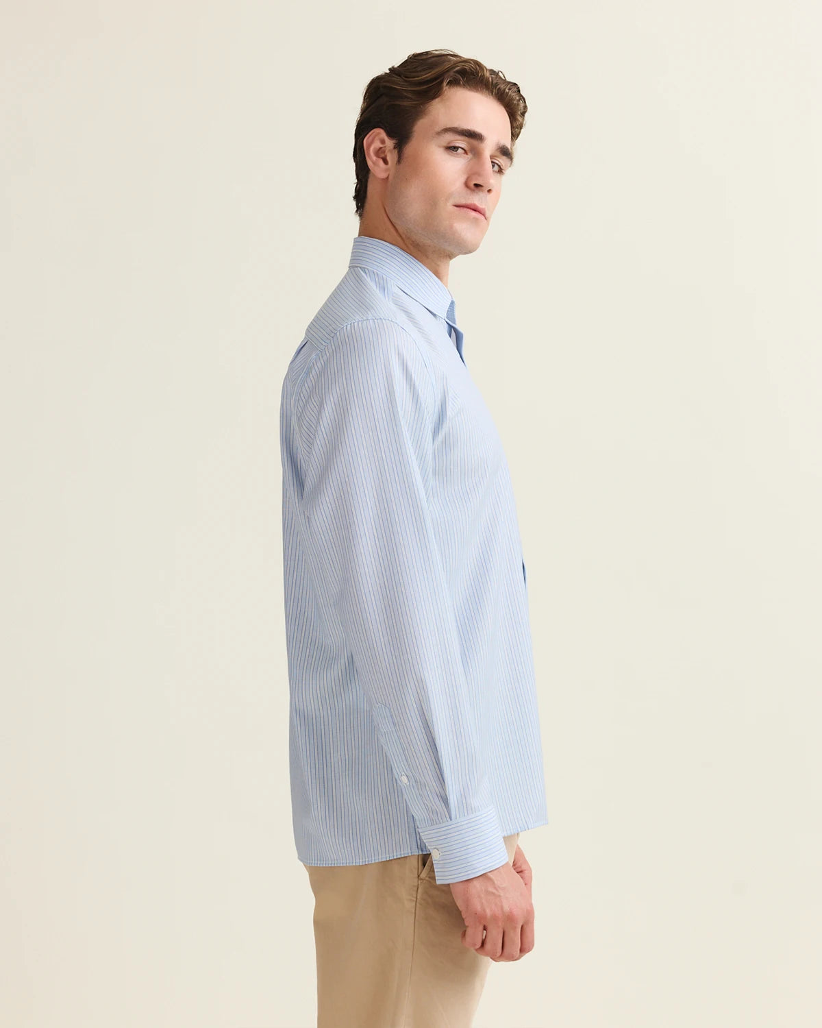 Side view of Man wearing a light blue striped merino shirt against a beige background