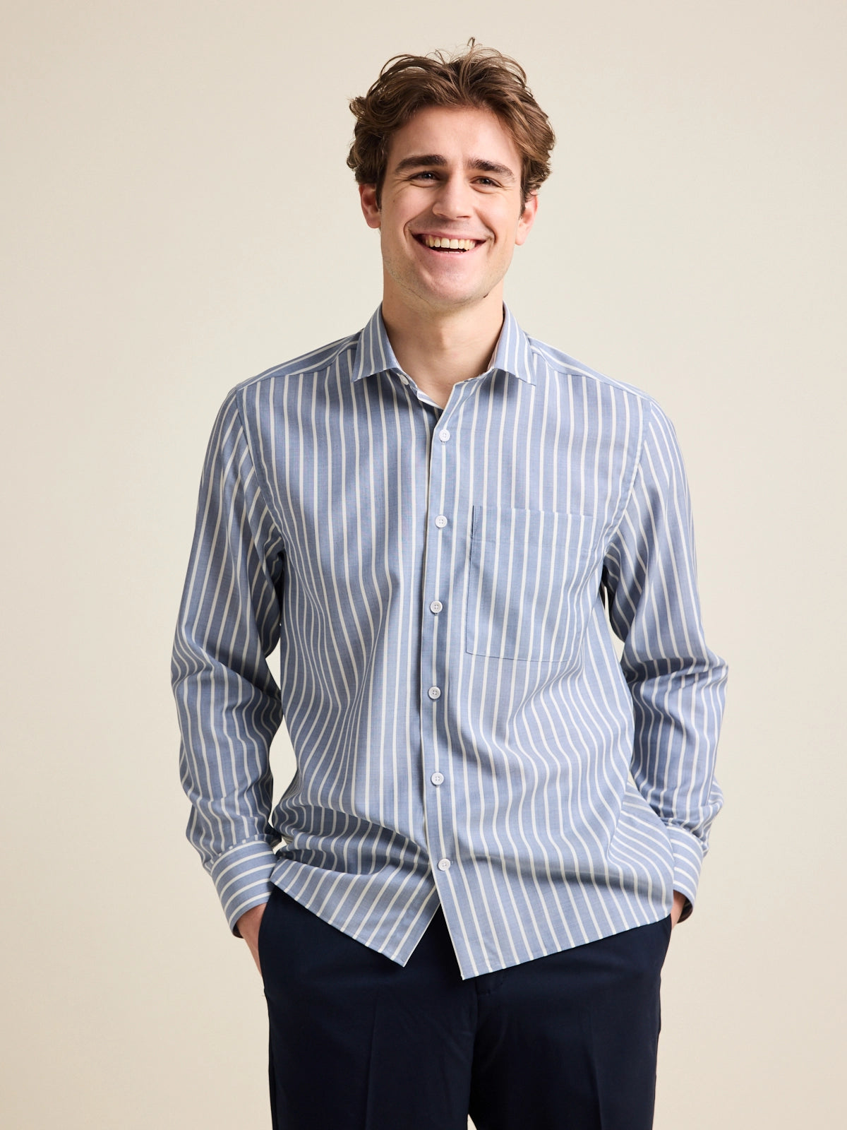 Man wears a merino wool shirt with long sleeves from Wolk. The merino shirt has a chest pocket and has a navy-white striped pattern. combined with navy pants.