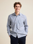 Man wears a merino wool shirt with long sleeves from Wolk. The merino shirt has a chest pocket and has a navy-white striped pattern. combined with navy pants.