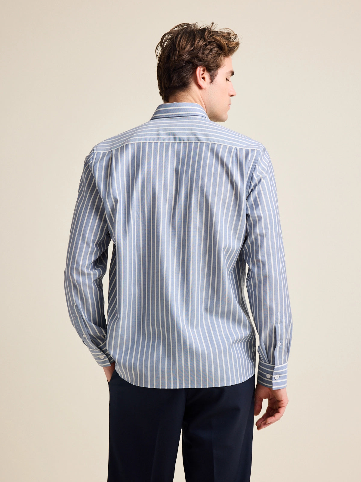Back view of model wearing a blue with striped merino wool shirt on navy pants.