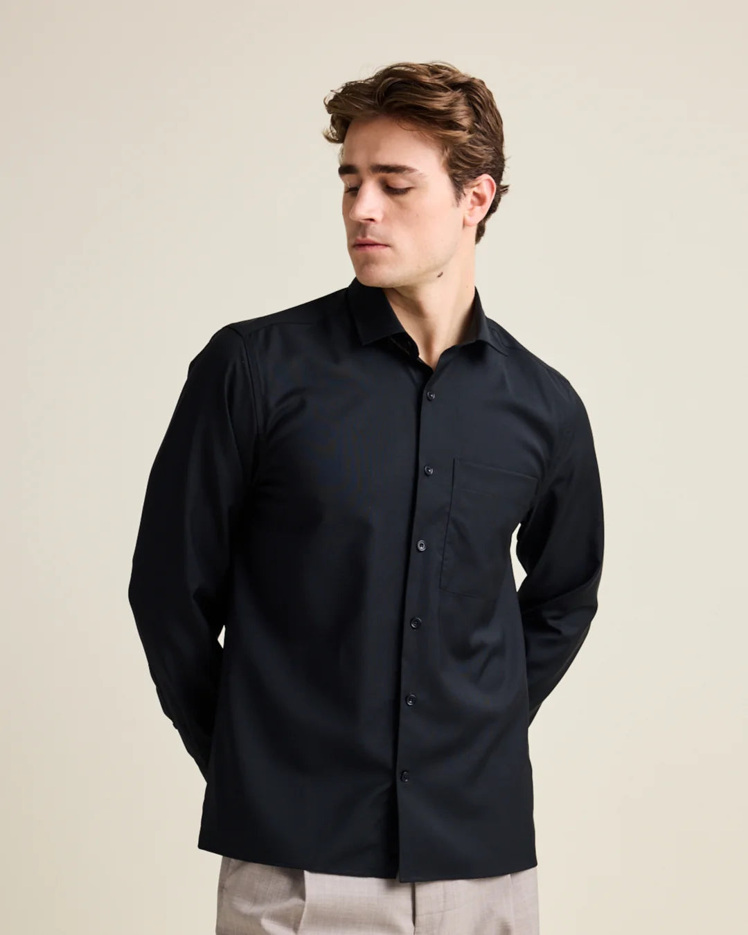 Man wearing a black relaxed merino wool shirt against a beige background