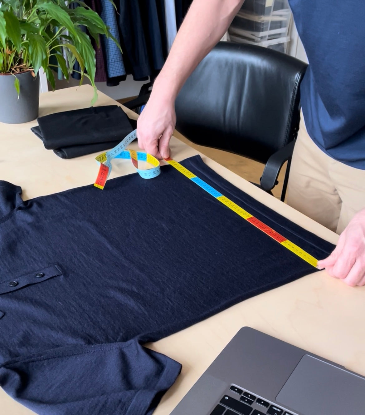 Person measuring a navy shirt on a table with a ruler Wolk merino wool garments are designed in Belgium