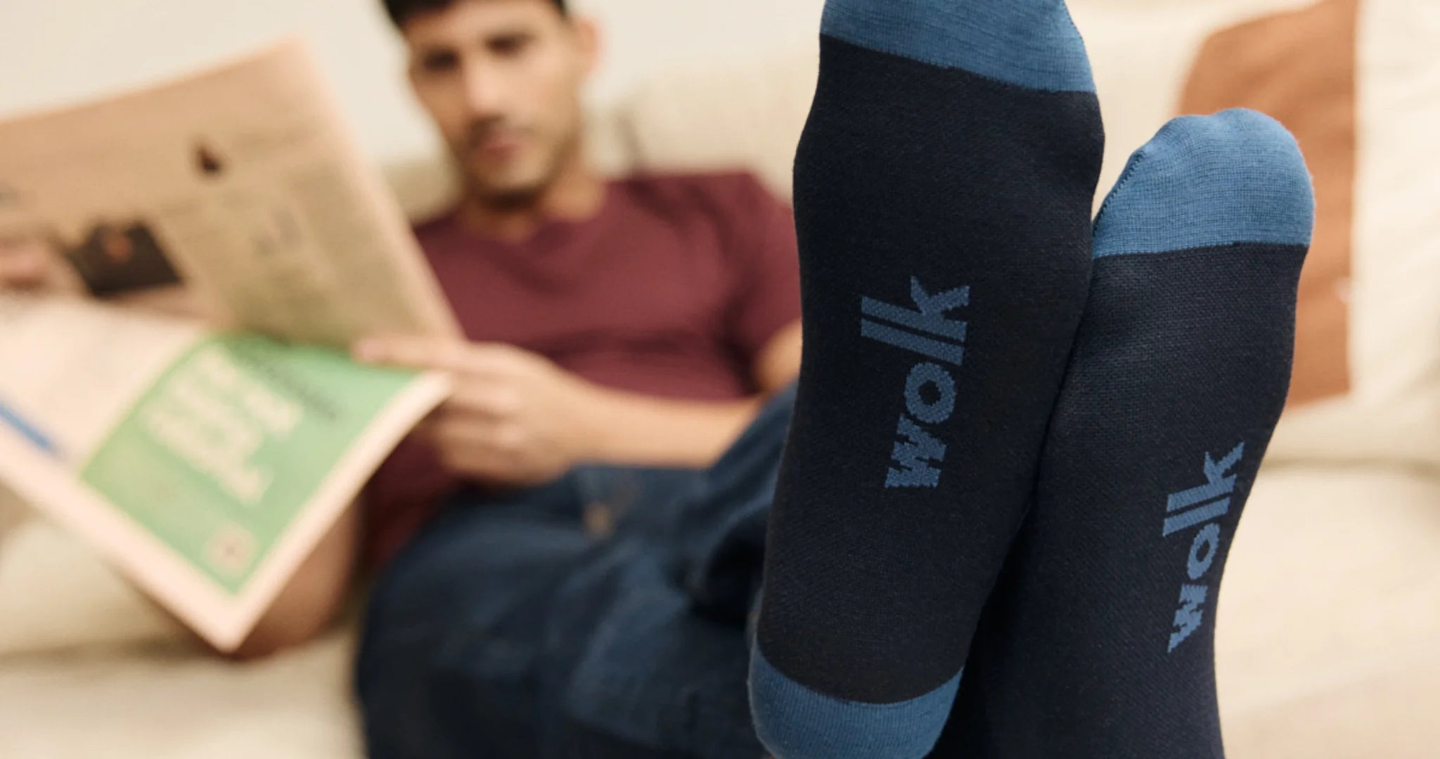 Person wearing merino wool socks with 'wolk' branding, sitting on a couch reading a magazine.
