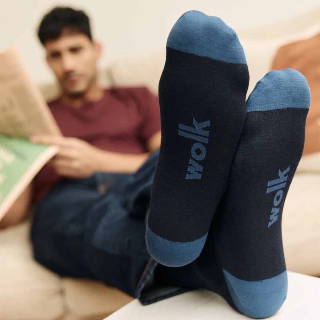 Person wearing Wolk navy merino wool socks with blue toes and heels, sitting on a couch reading a book.