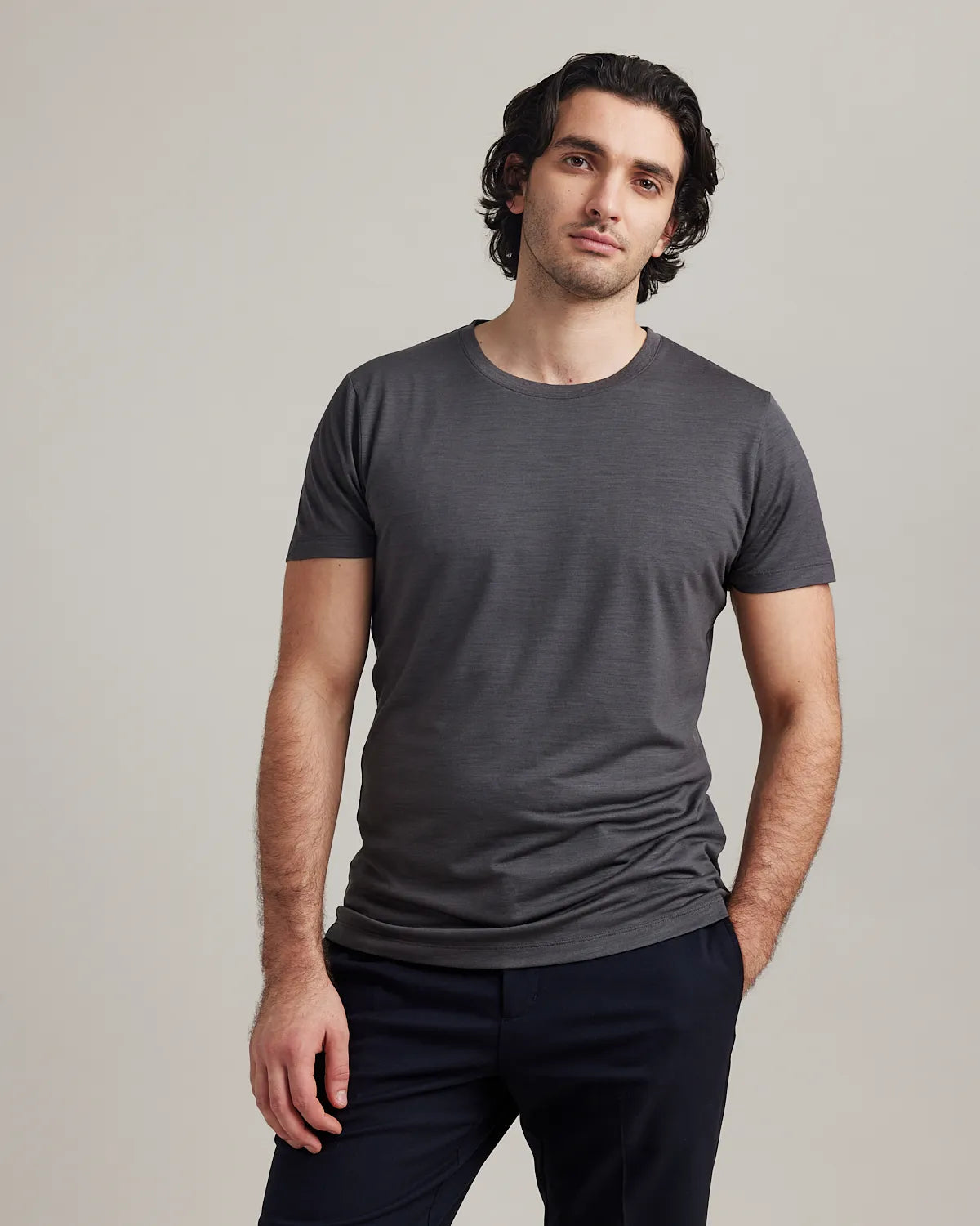 Man wearing a dark gray merino t-shirt and black pants against a plain background