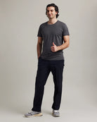 Man wearing a gray merino t-shirt and dark navy pants on a plain background