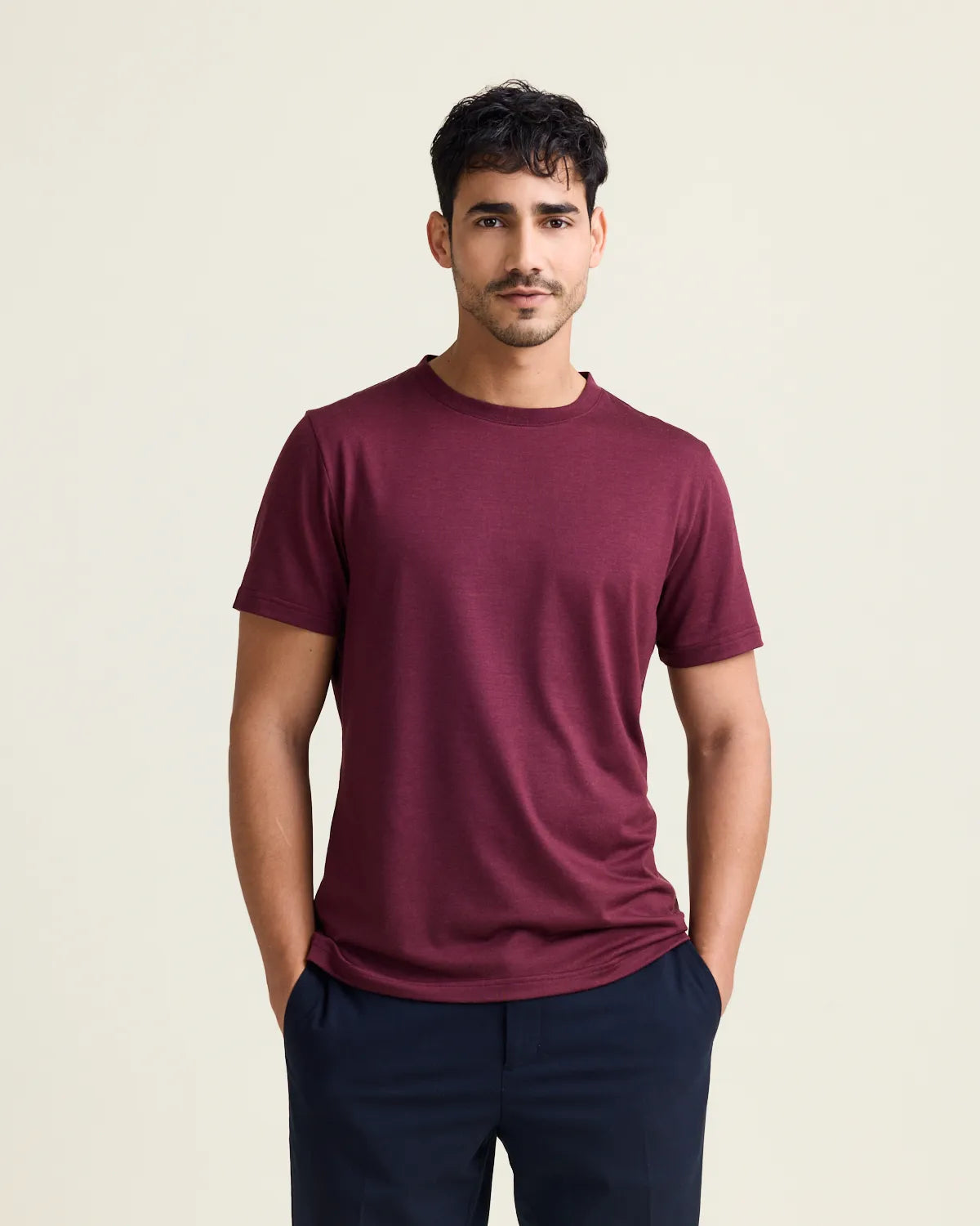 Man wearing a burgondy merino t-shirt and dark pants on a beige background