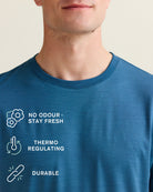 Wolk's blue merino T-shirt collar detail with benefit icons: no odour, thermo-regulating and durable.