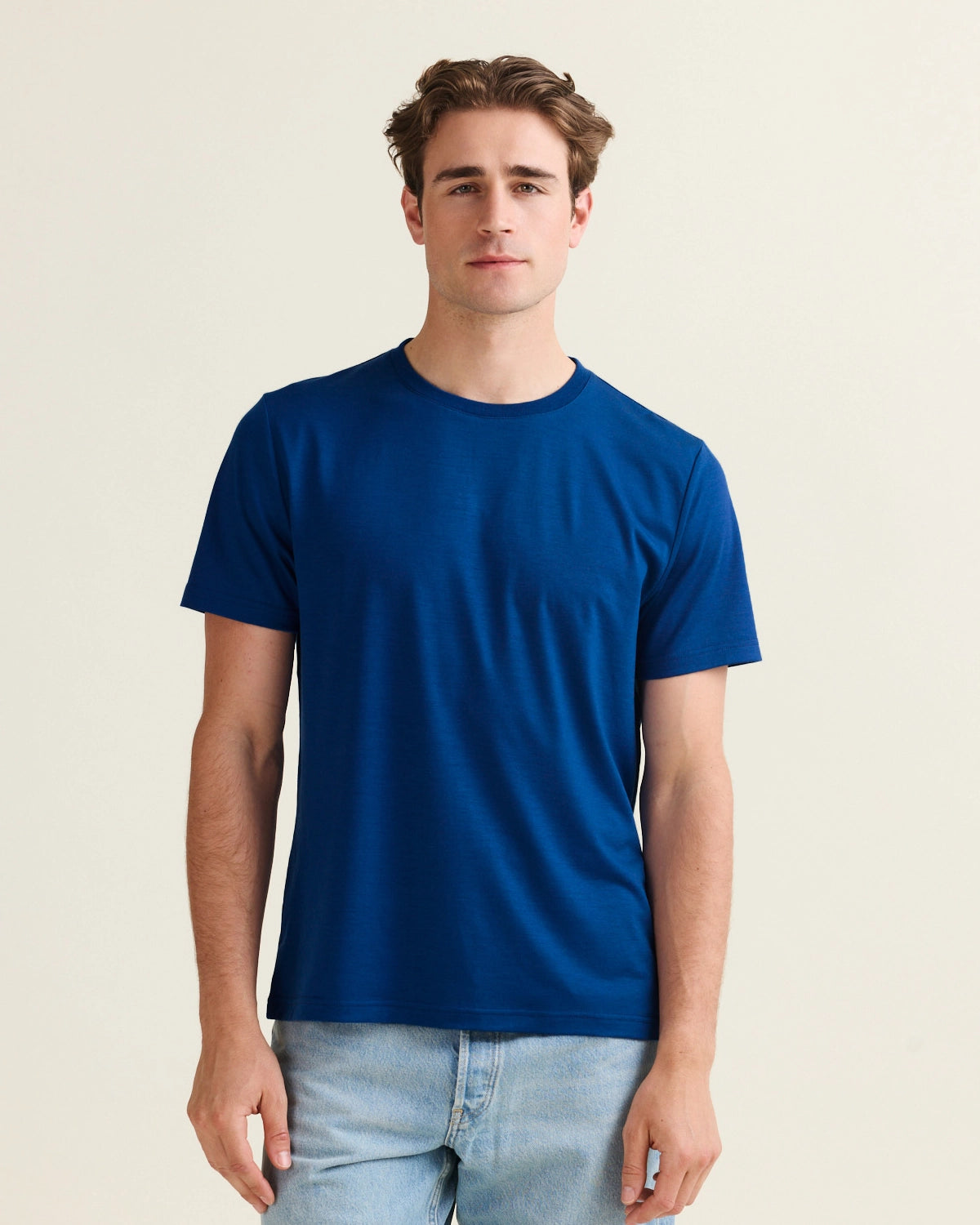 Man wearing a blue merino wool t-shirt on a jeans against a beige background