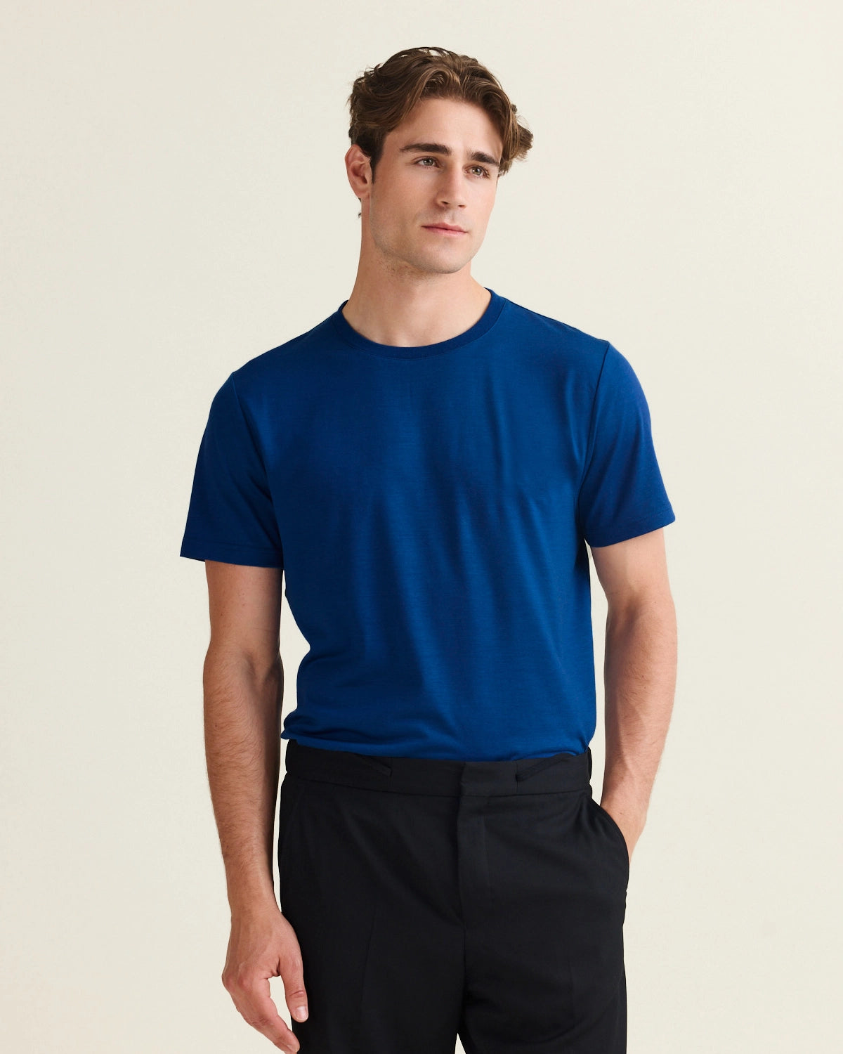 Man wearing a stylish blue merino wool t-shirt and black pants on a beige background