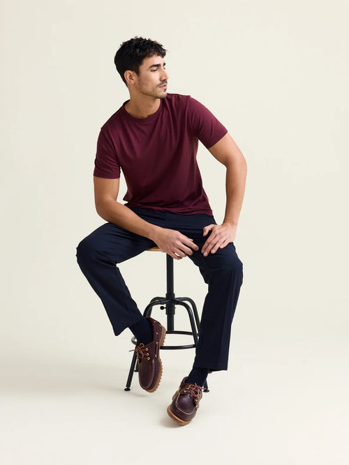 man sits on chair with navy pants and burgundy colored merino T-shirt with shirt sleeves from Wolk