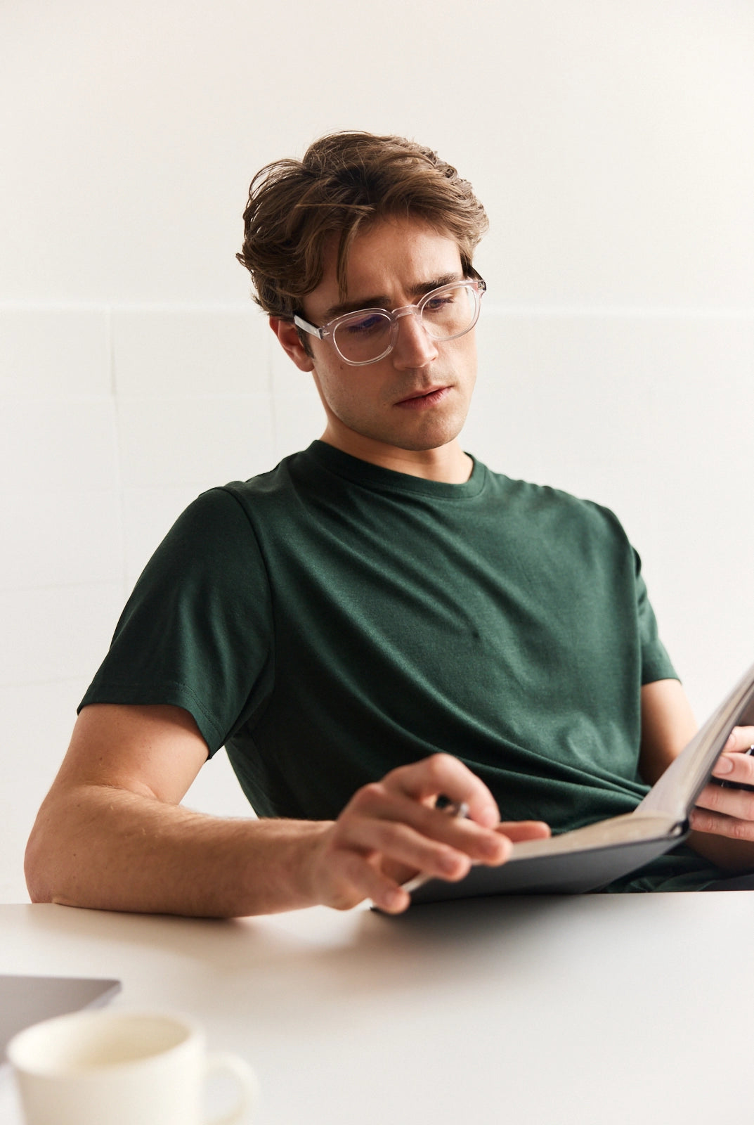 Man wearing a dark green merino wool T-shirt with short sleeves sitting in an office