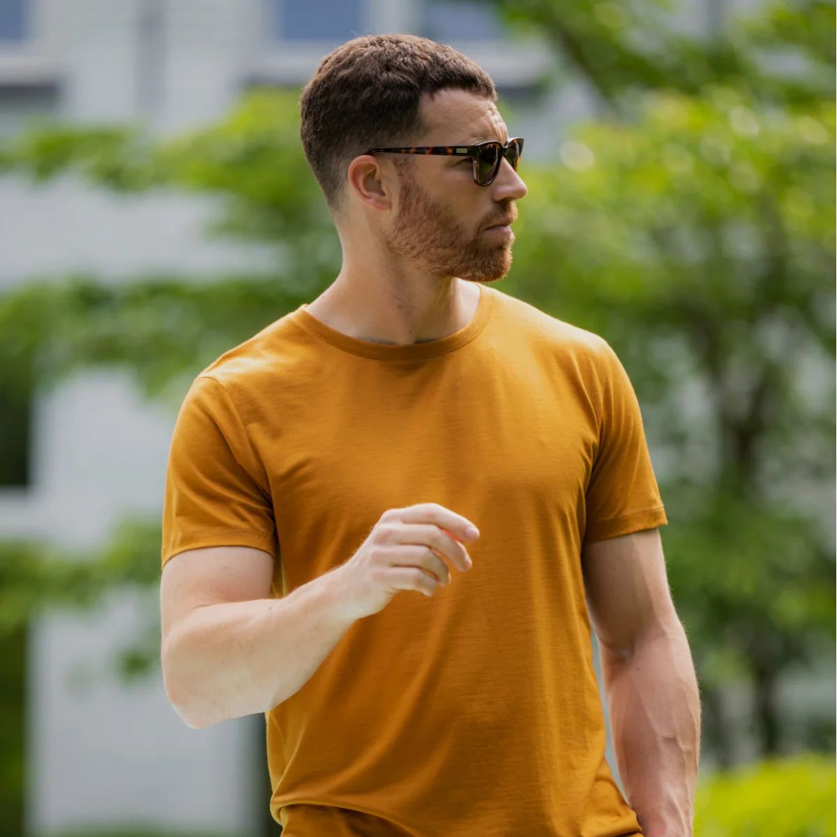 Man wearing a mustard yellow merino wool  t-shirt outdoors with greenery in the background
