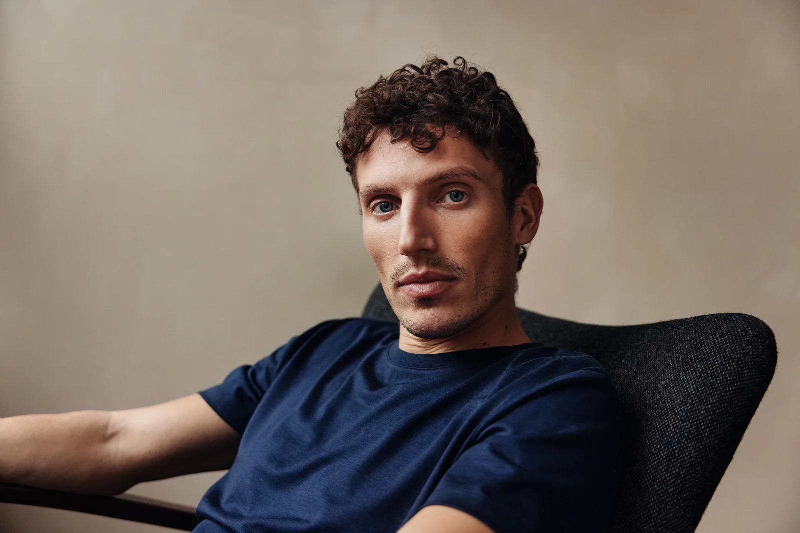 Man sits in chair and wears a navy merino wool T-shirt from Wolk