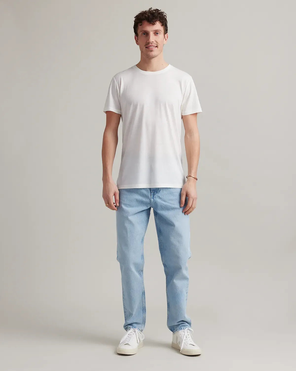 Man wearing a white merino t-shirt and light blue jeans on a plain background
