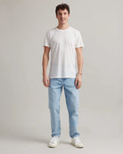 Man wearing a white merino t-shirt and light blue jeans on a plain background