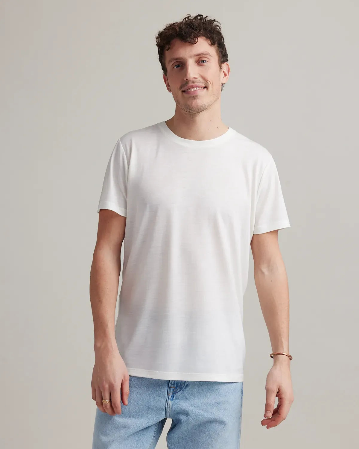 Man wearing a plain white merinowool t-shirt and light blue jeans against a neutral background